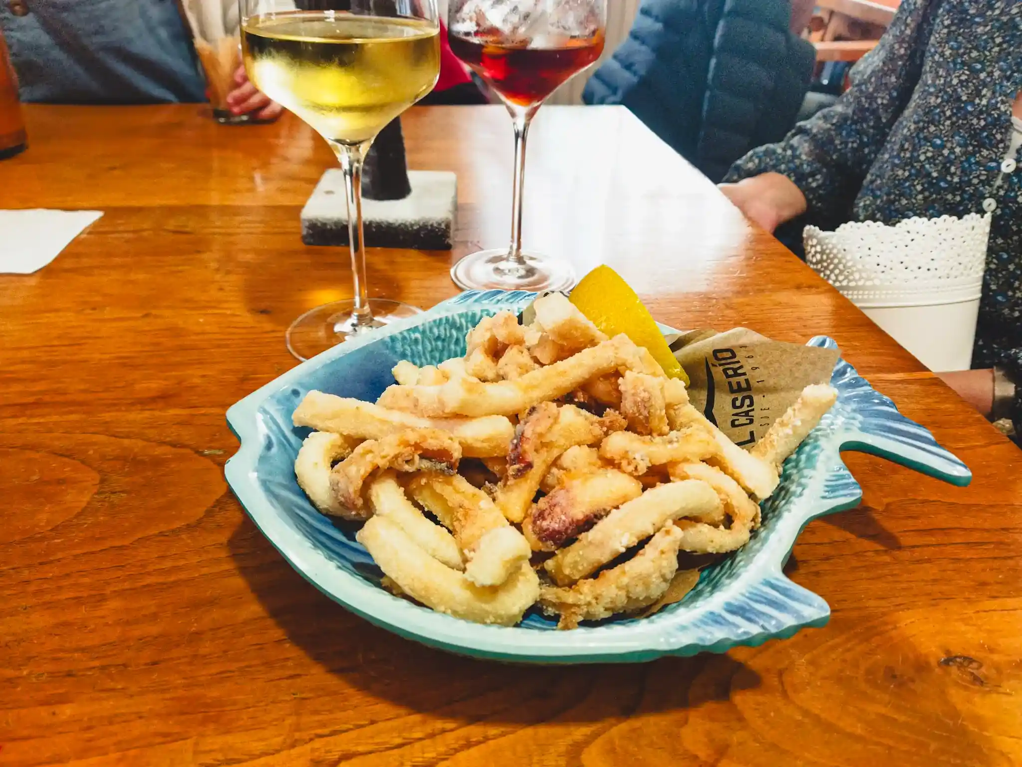 Rabas sin gluten en un plato azul con forma de pez y dos copas de vino al fondo