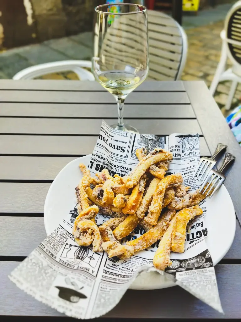 Plato de rabas sin gluten servidas sobre papel de periódico junto a una copa de vino blanco