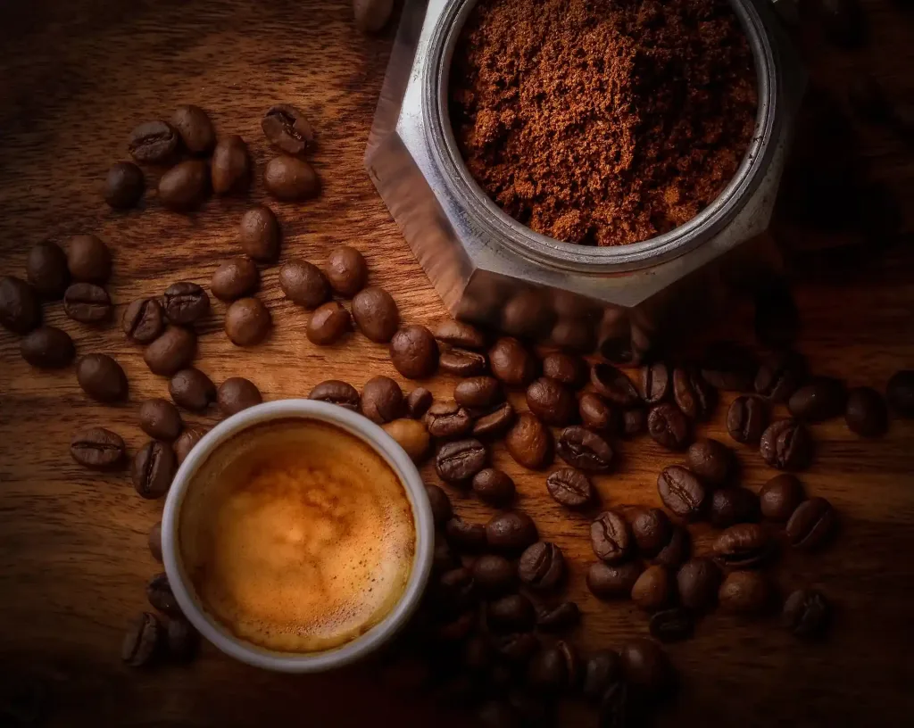 Taza de café sobre madera, granos de café y cafetera italiana abierta con café molido