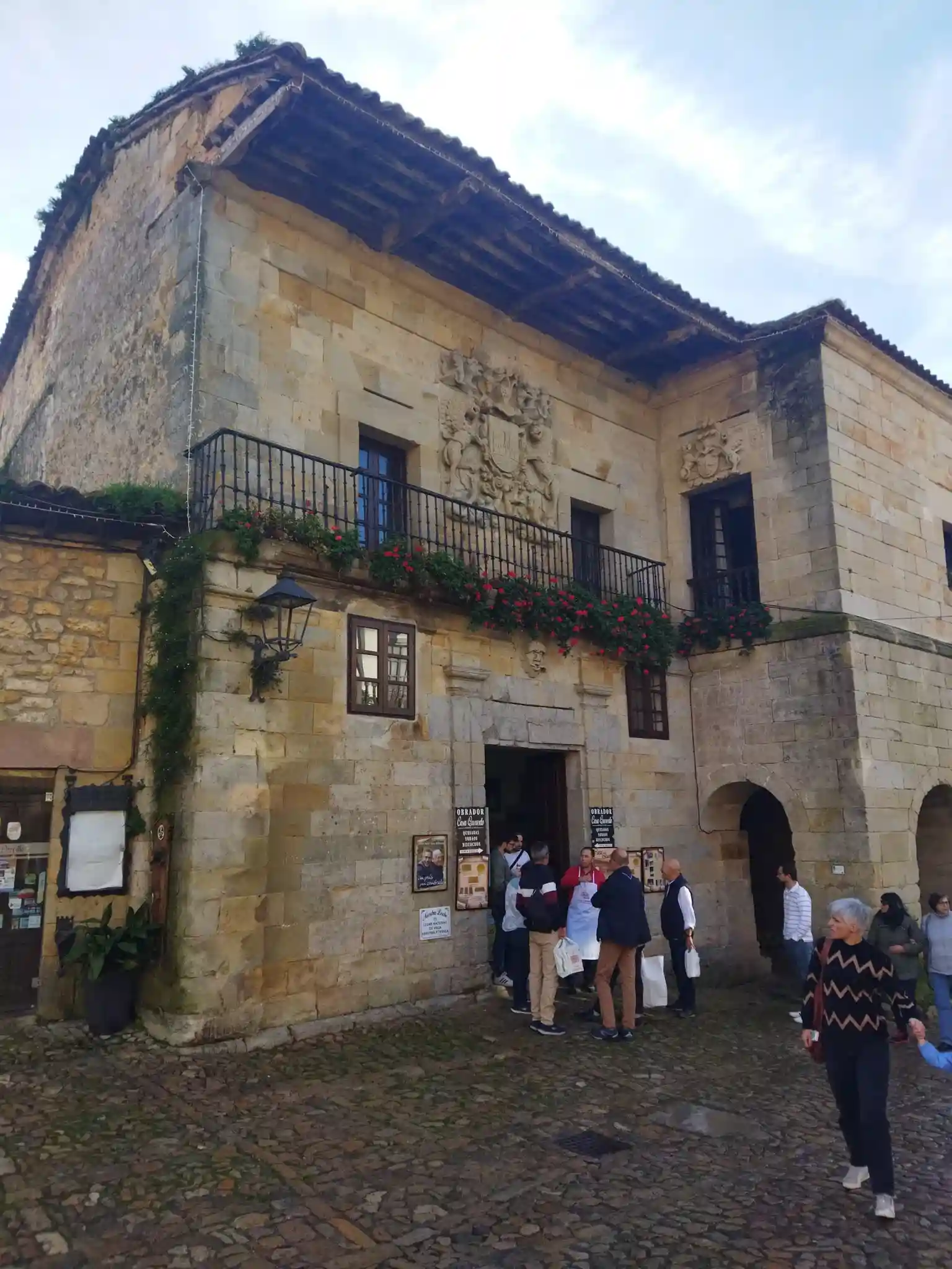 Edificio de piedra de sillería con gente tomando un sobao y leche en Santillana del Mar