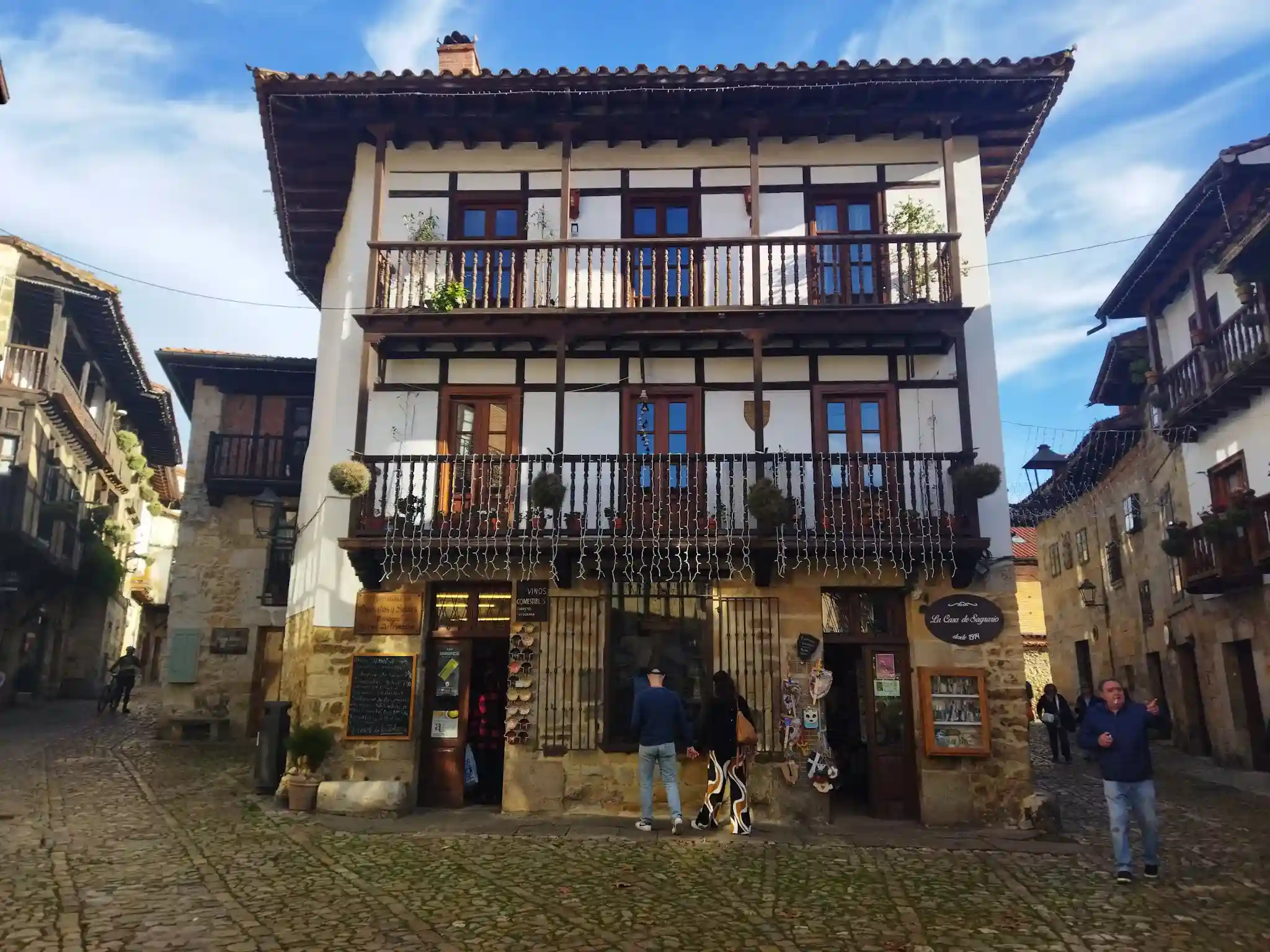 Edificio de piedra de sillería de color blanco con tiendas en la planta baja y gente paseando en Santillana del Mar