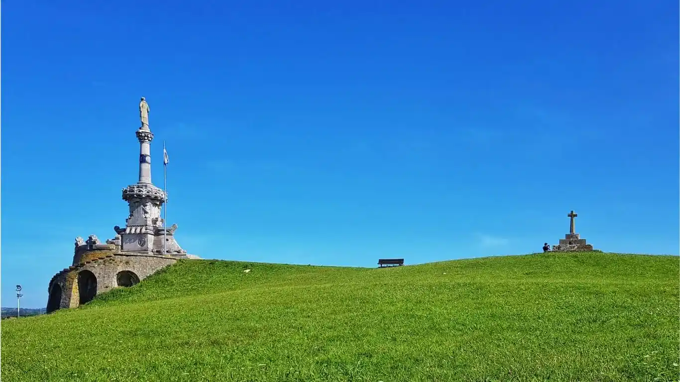 Monumento en lo alto de una colina de color verde con el cielo azul