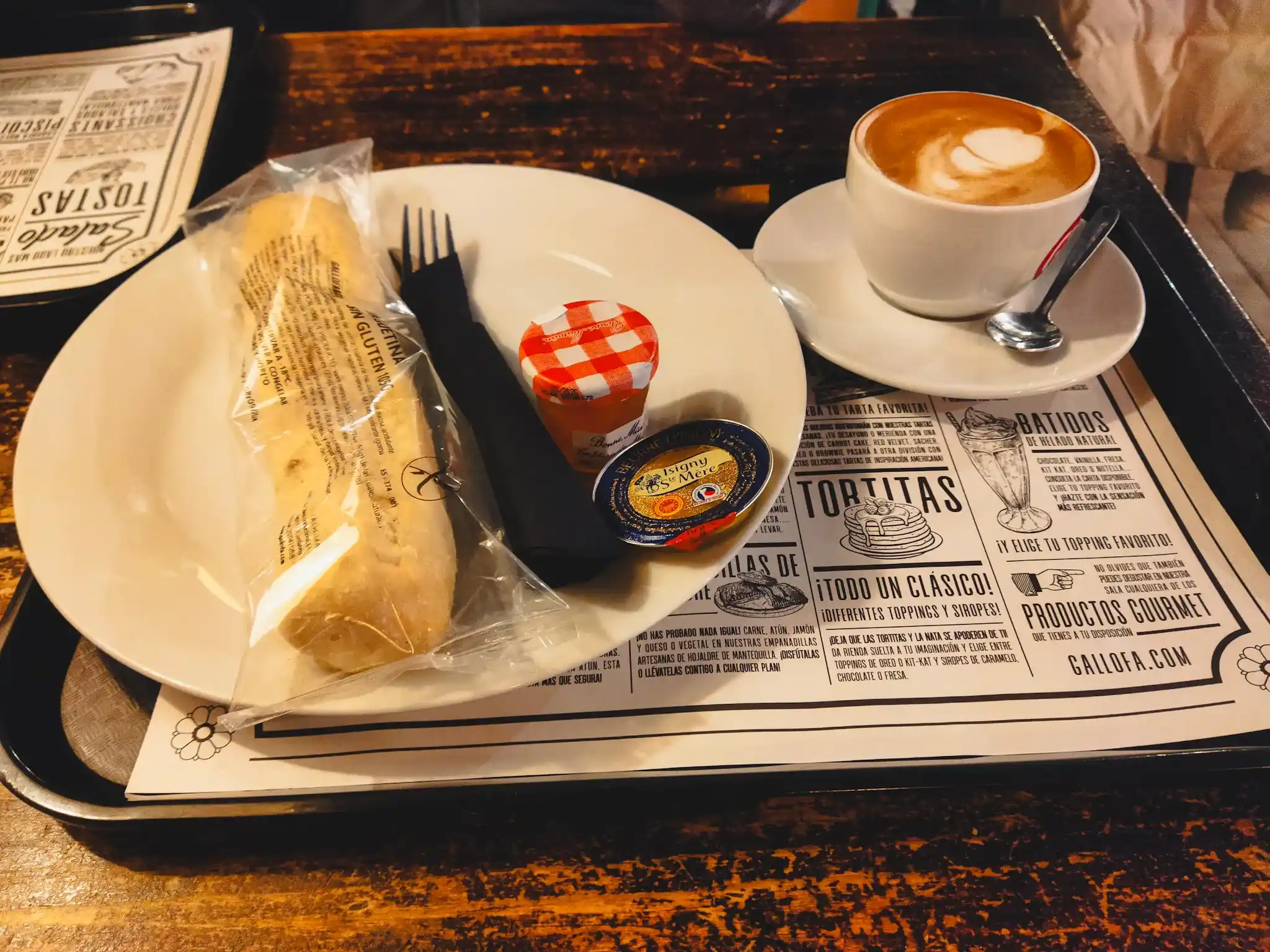 Plato con pan sin gluten envasado, un café y mantequilla con un bote pequeño de mermelada