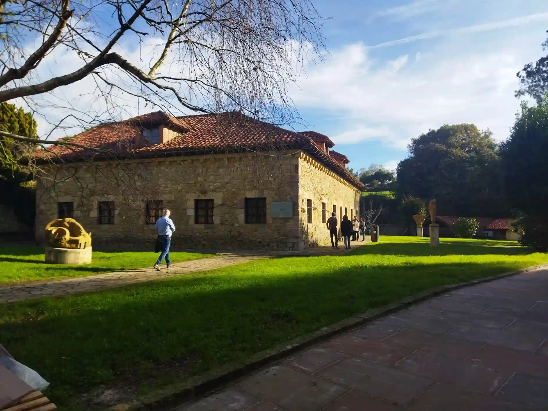 Jardín muy verde con un árbol sin hojas en el primer plano y un edificio bajo de piedra en Santillana del Mar