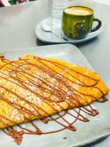 Crepe sin gluten con chocolate por encima y un café en una taza verde