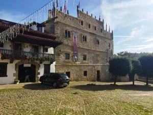 Palacio señorial de piedra de silleria con un coche a la entrada y suelo empedrado en Santillana del Mar