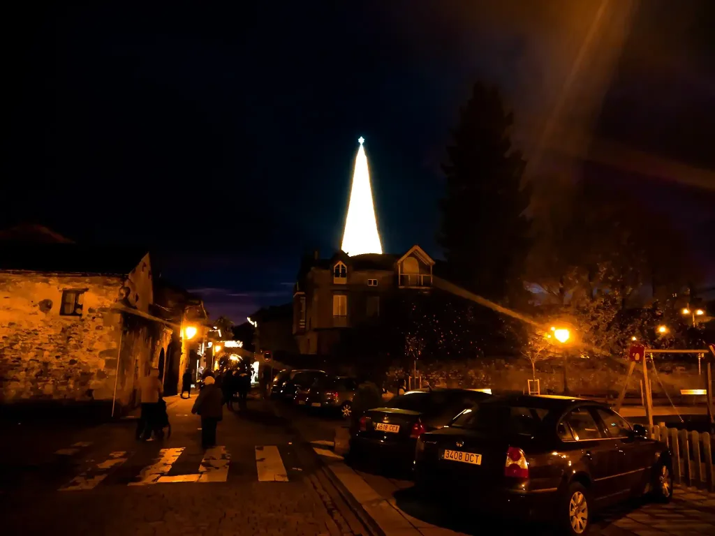 Conjuntos de edificios de piedra con algún coche en el primer plano. Al fondo se ve un árbol iluminado de Navidad gigantesco. Navidad Cantabria.