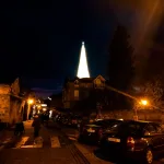 Conjuntos de edificios de piedra con algún coche en el primer plano. Al fondo se ve un árbol iluminado de Navidad gigantesco. Navidad Cantabria.