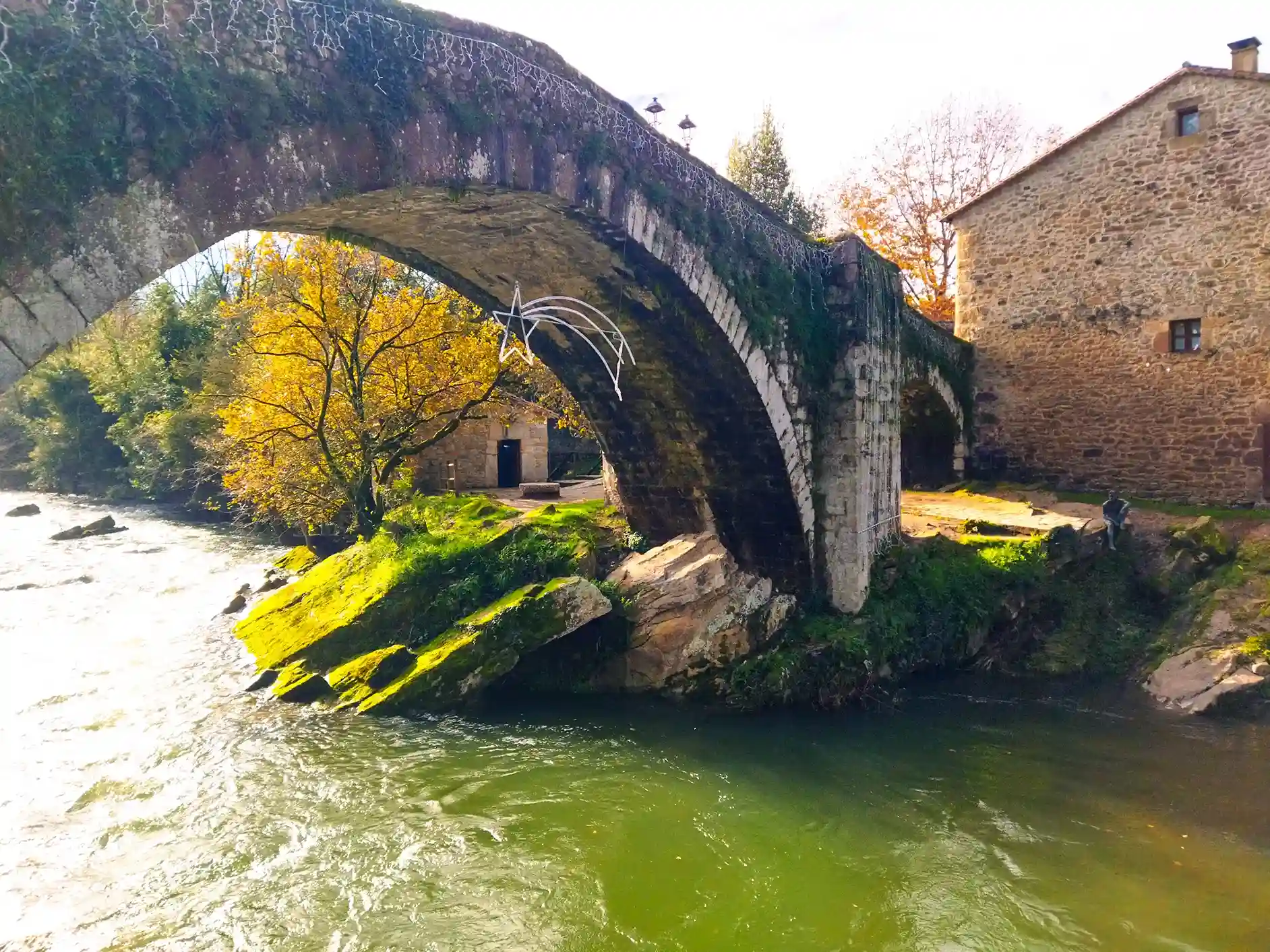 Puente medieval con el río pasando por debajo y una estatua de bronce de un hombre pez de Liérganes