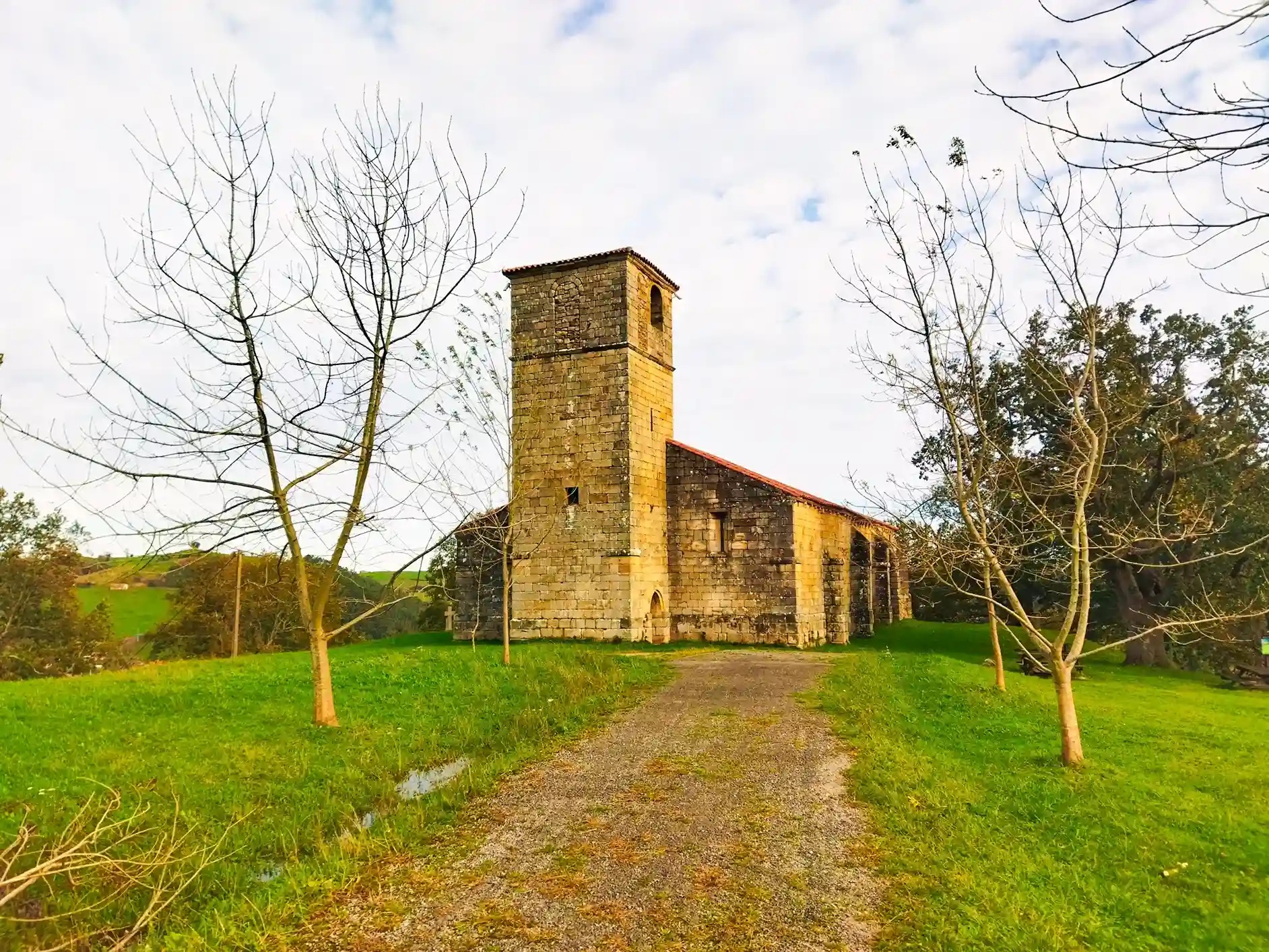 Iglesia de piedra en el fondo y un camino de tierra hacia ella