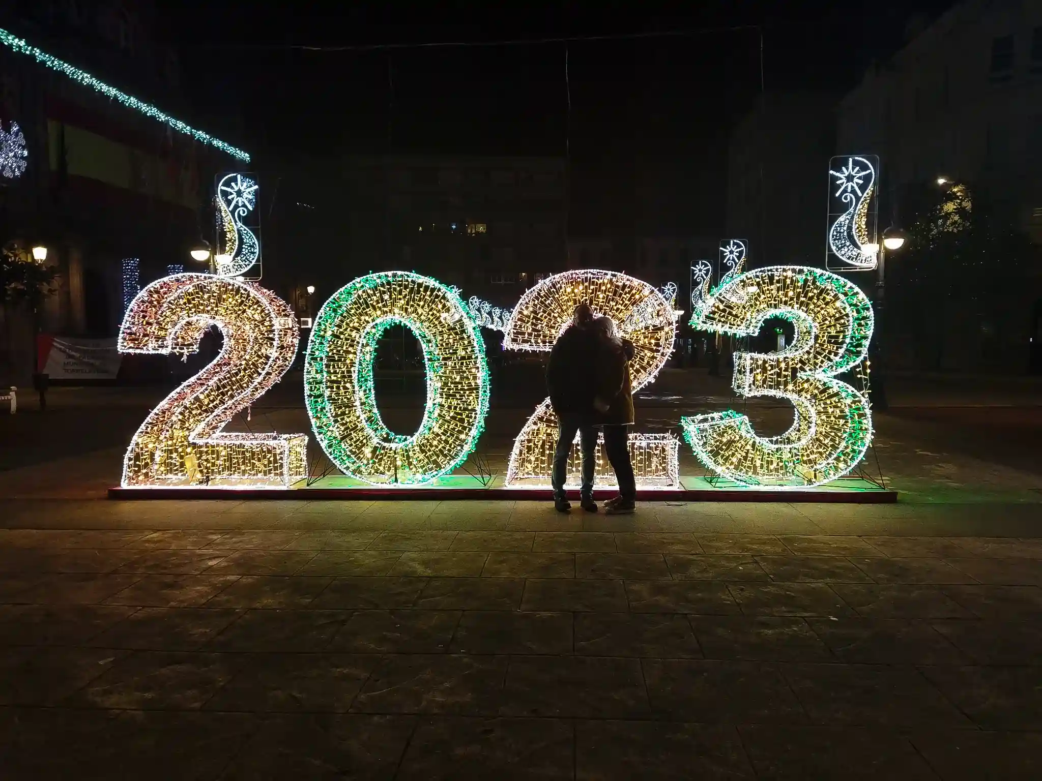 Año 2023 iluminado con luces de Navidad con dos personas delante. 