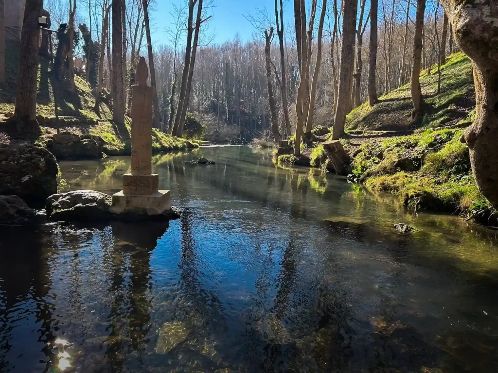río con árboles a los lados y una estatua de una virgen a la izauierda