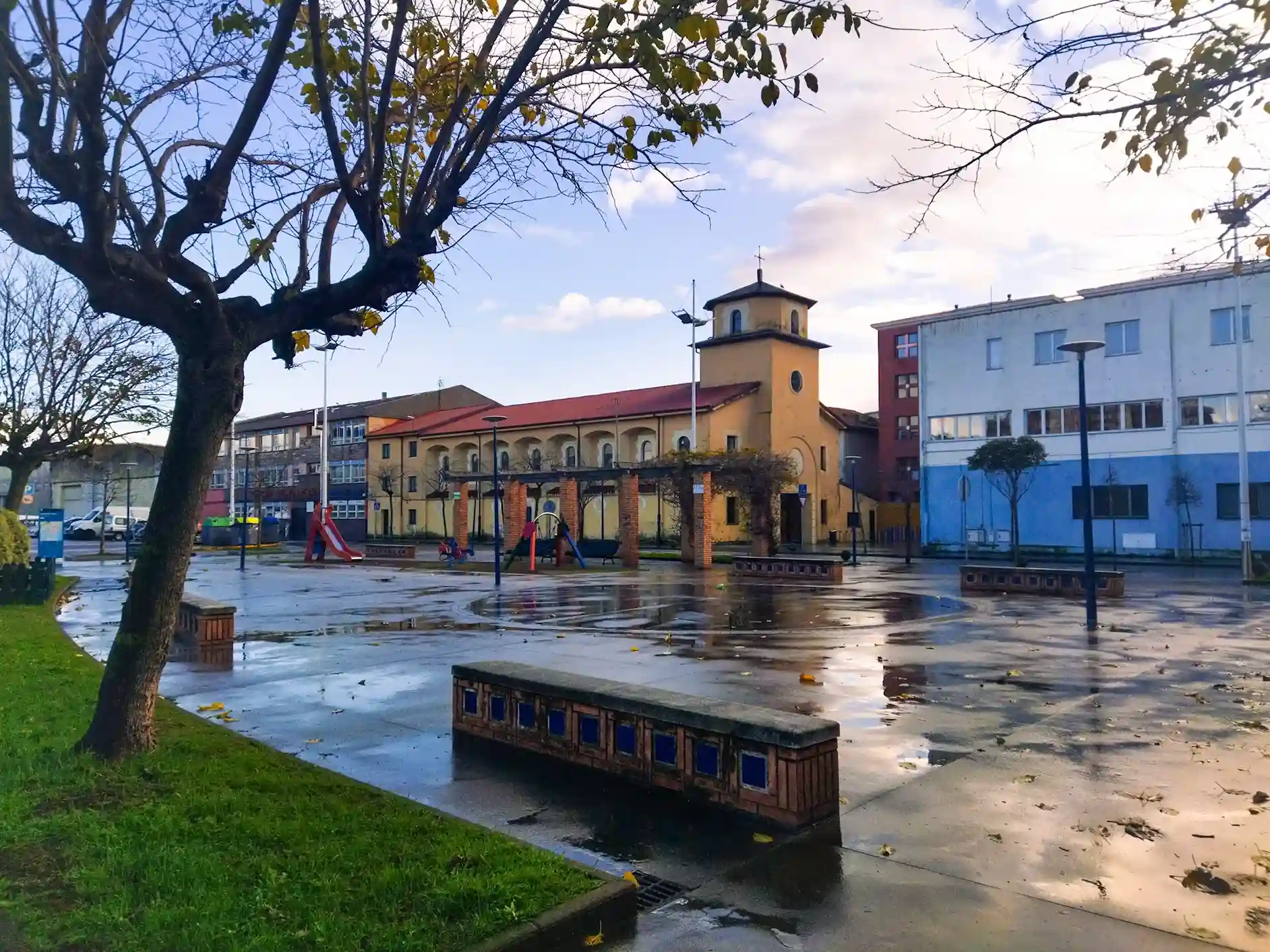 Iglesia de color beige con edificios rodeándola y un árbol en el primer plano