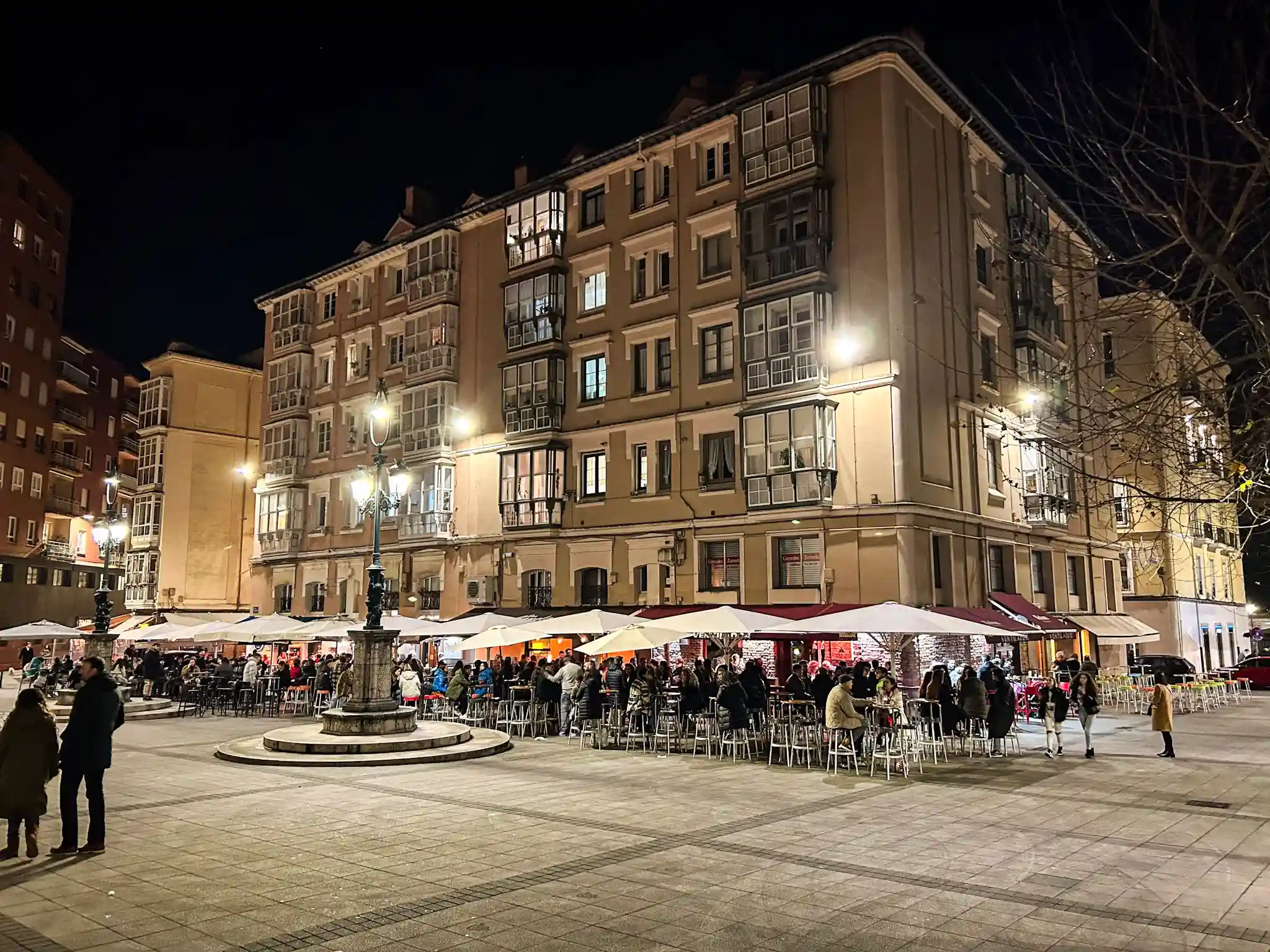 Plaza con edificios a los lados y gente tomando copas
