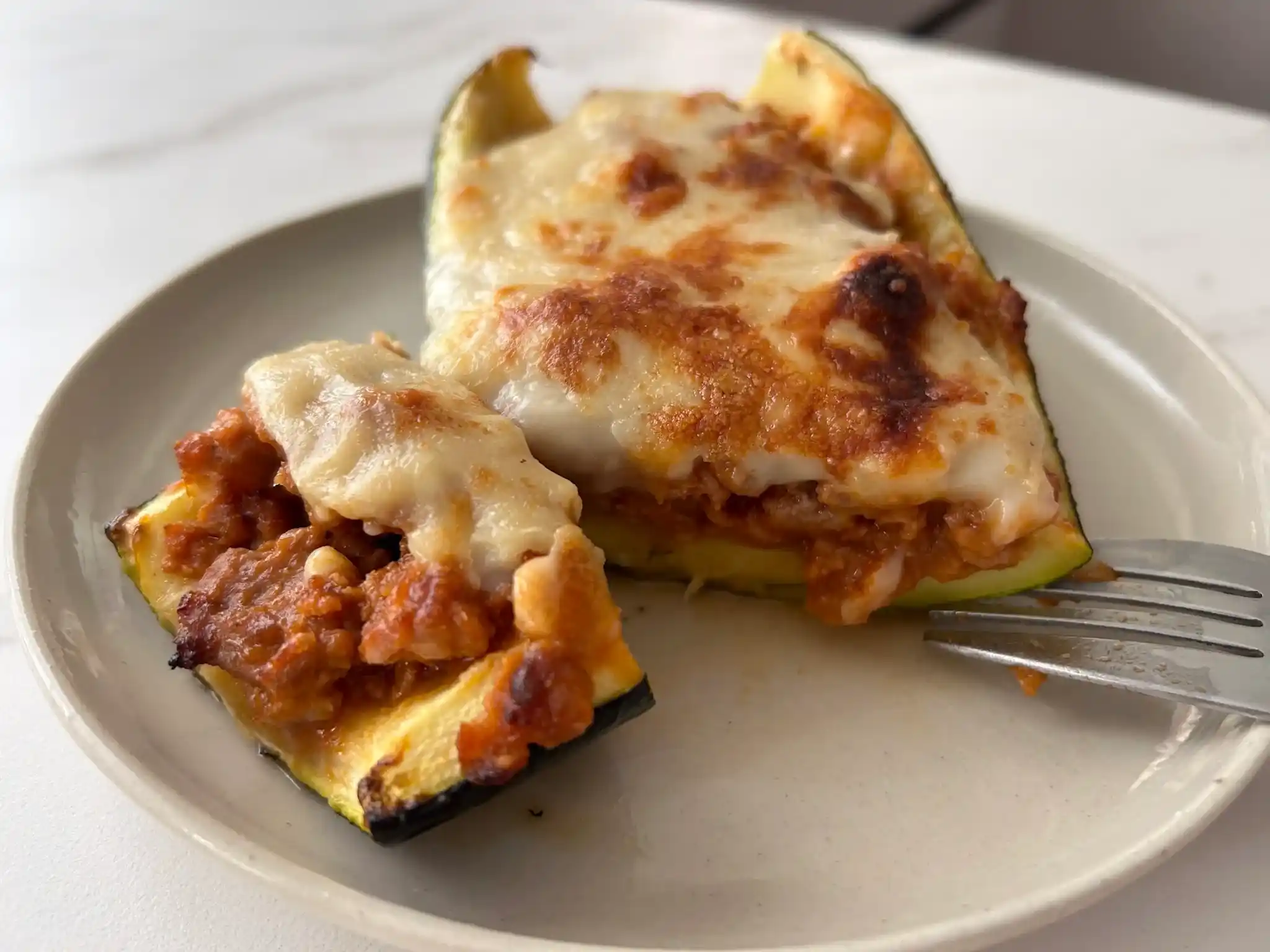 calabacines rellenos de carne con queso en un plato pequeño y con un tenedor