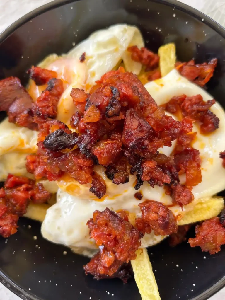 Huevos fritos con jijas y patatas fritas en una sartén negra